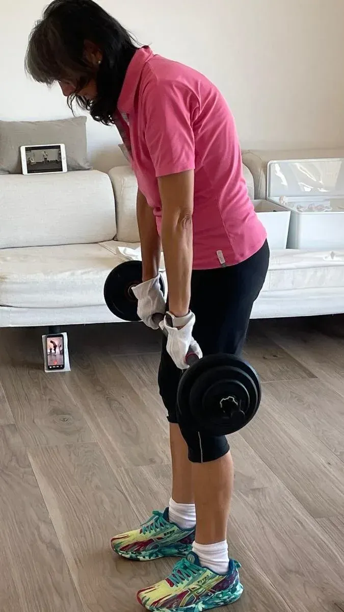Alumna del programa entrenando con mancuernas en el salón de su casa