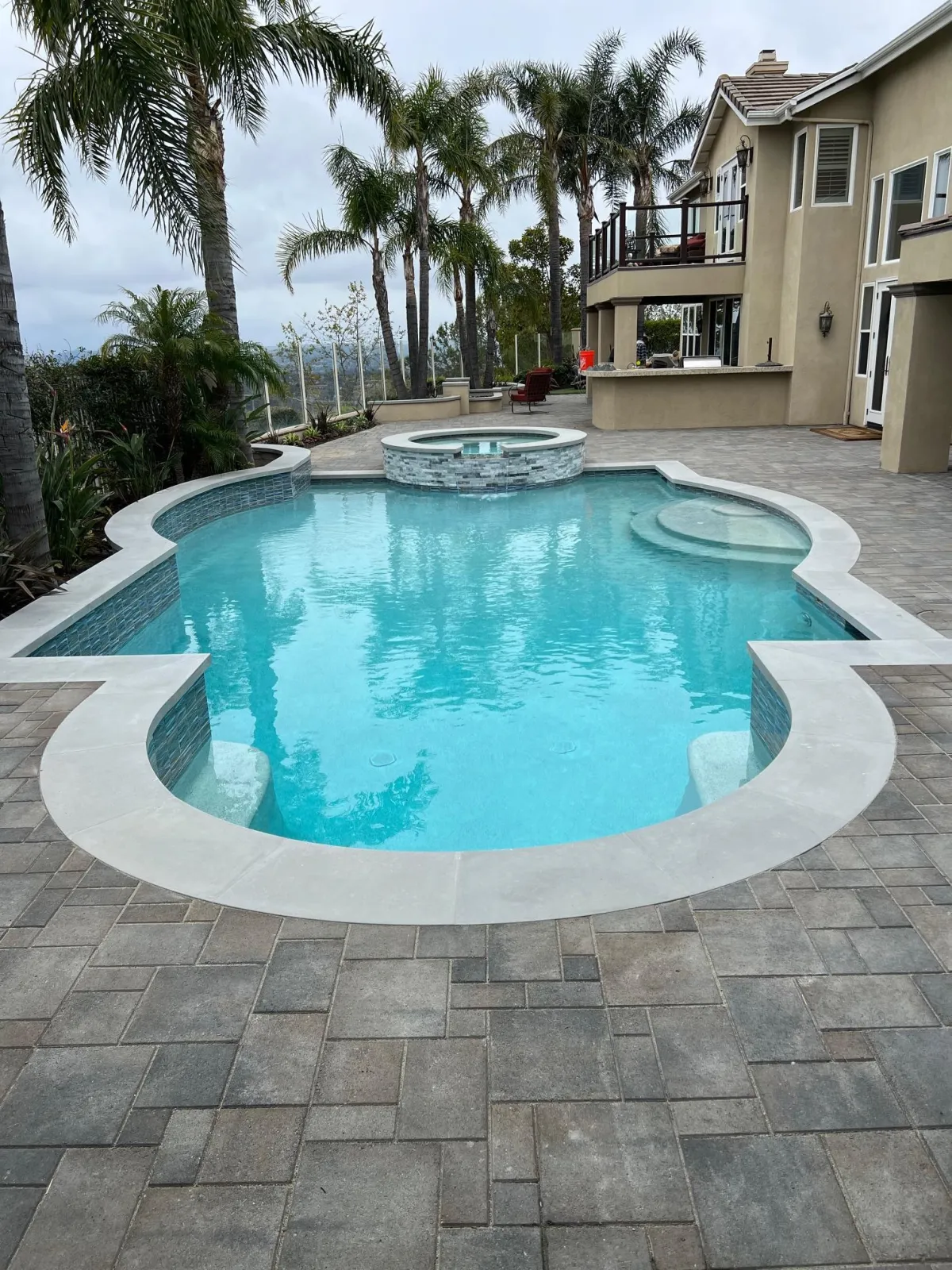 Interlocking paver installation in a backyard surrounding a pool with concrete coping.