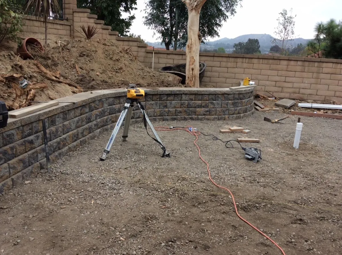 Short block retaining wall installed in a backyard, creating a planter on one side.