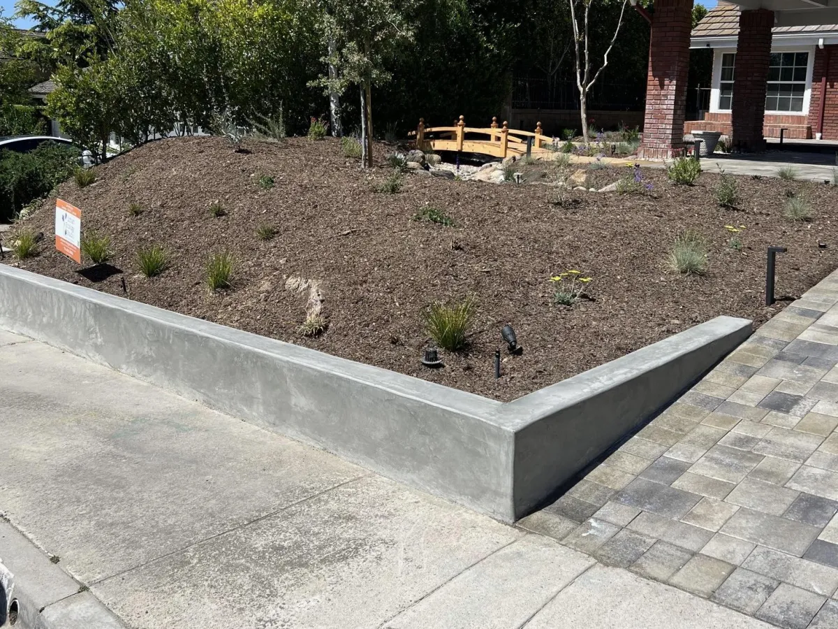 Short concreteretaining wall installed in a backyard, creating a planter on one side.