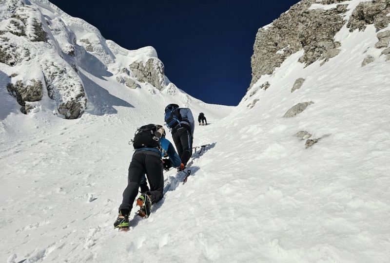 A group of people mountain climbing on a steep snowy slope.