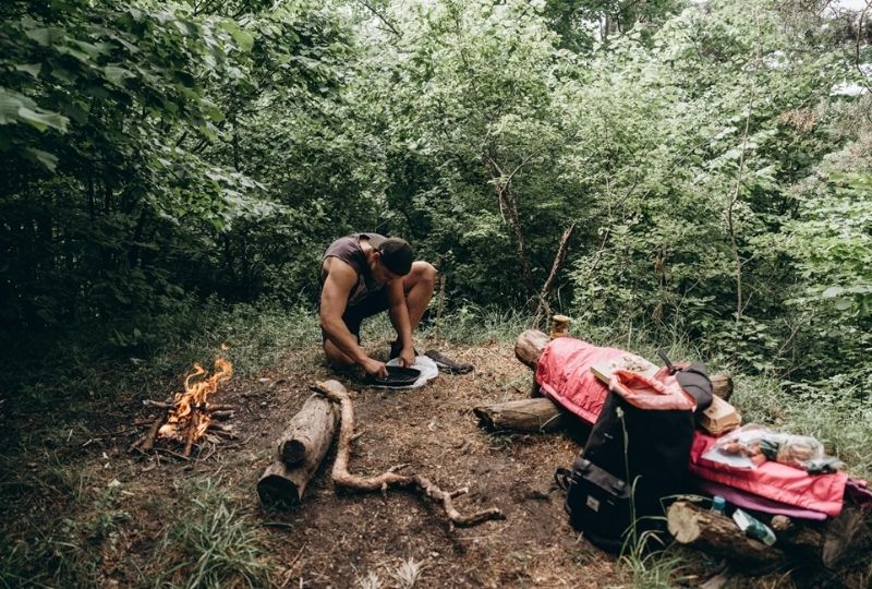 A man sitting beside a small campfire in the woods.