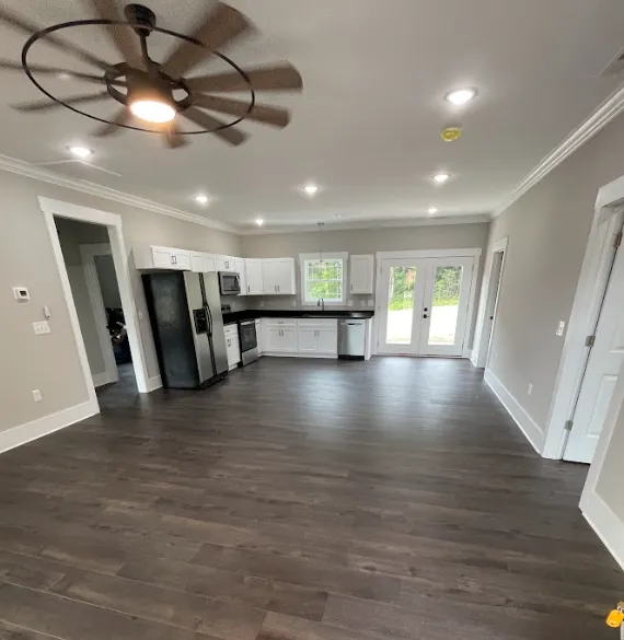 Contemporary kitchen with white shaker cabinets, stainless steel appliances, dark wood floors, and natural light from French doors and a central window.