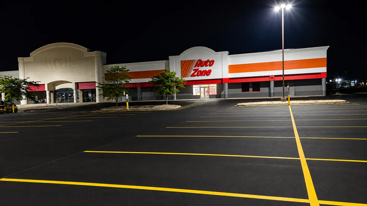 Freshly sealcoated commercial parking lot with bright yellow striping outside a retail building at night.