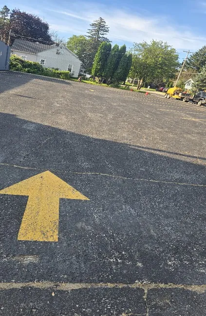 Asphalt parking lot with faded pavement markings and a yellow directional arrow