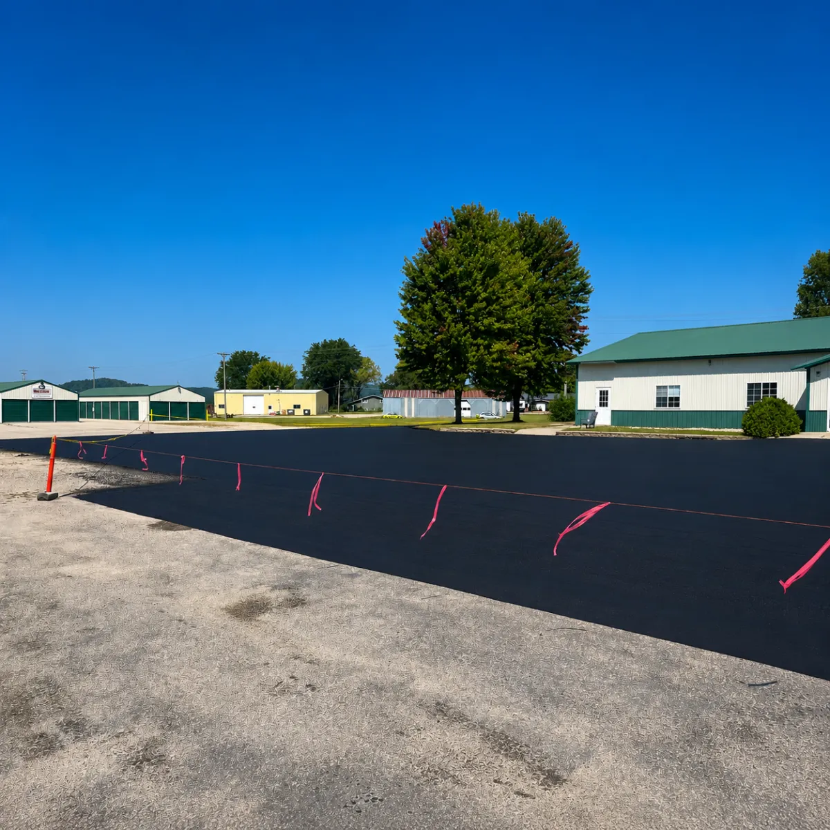 Freshly seal coated commercial asphalt parking lot beside an industrial building