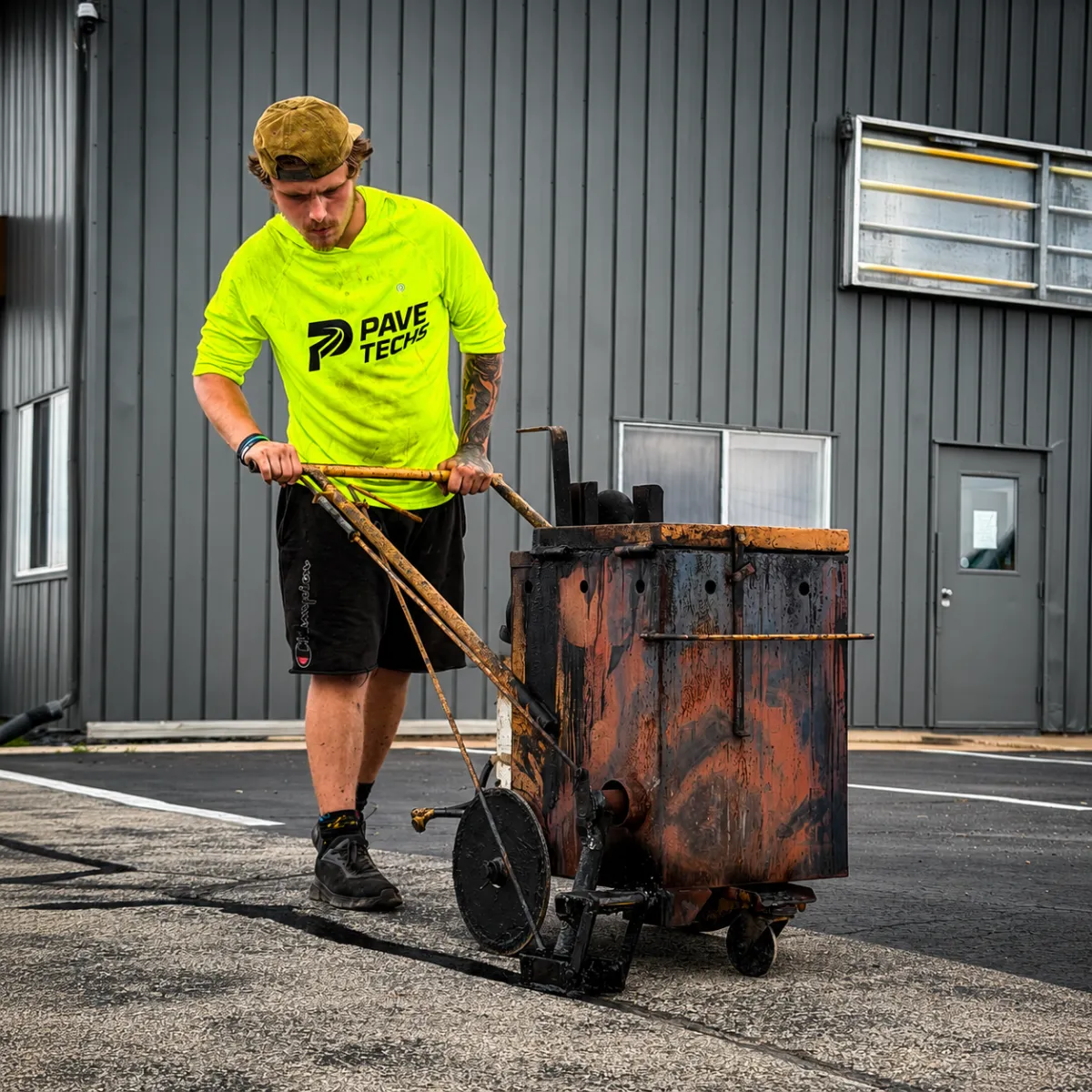 PaveTech Solutions worker applying hot crack sealant to asphalt pavement with a crack sealing machine