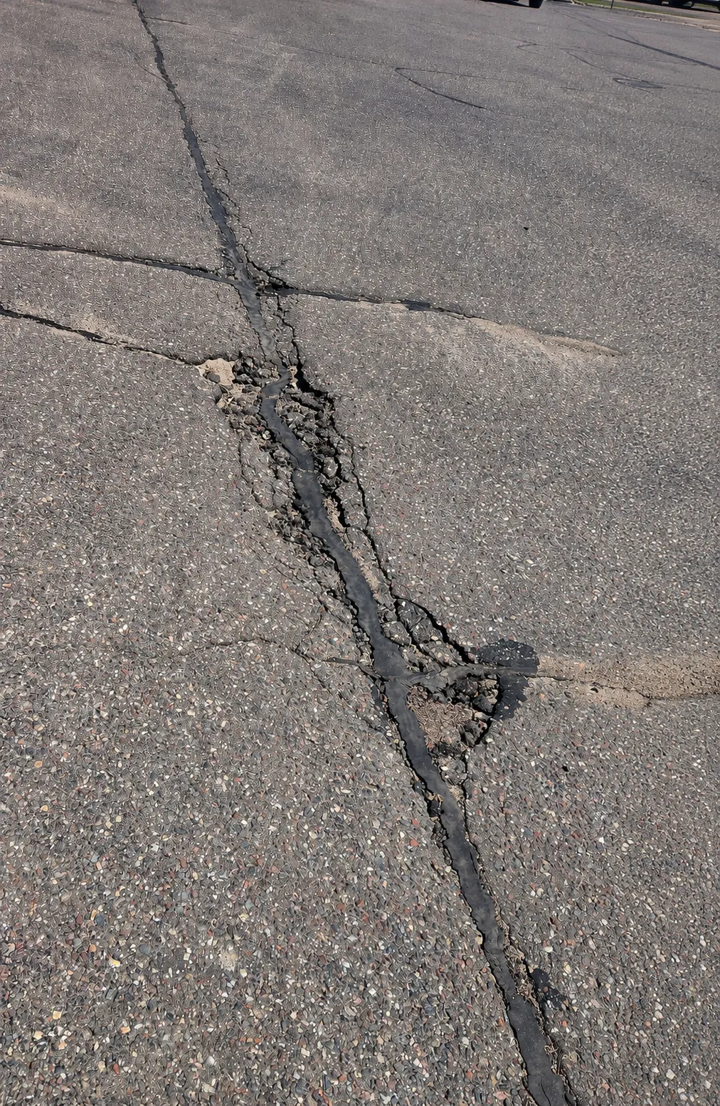 Failed asphalt crack seal with widened pavement damage and loose material along the repair line