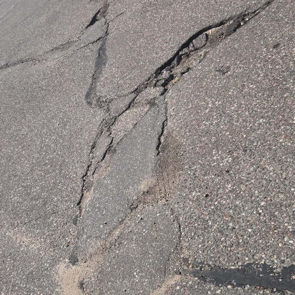 Severely deteriorated asphalt with a wide failed crack and previous crack repair material