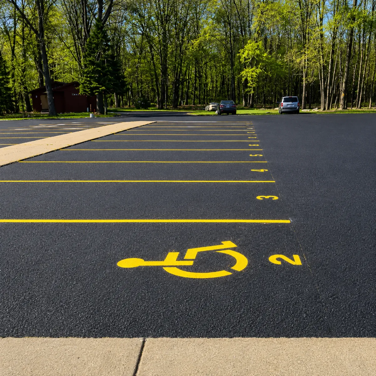 Fresh yellow ADA parking markings and numbered parking spaces on a paved parking lot.
