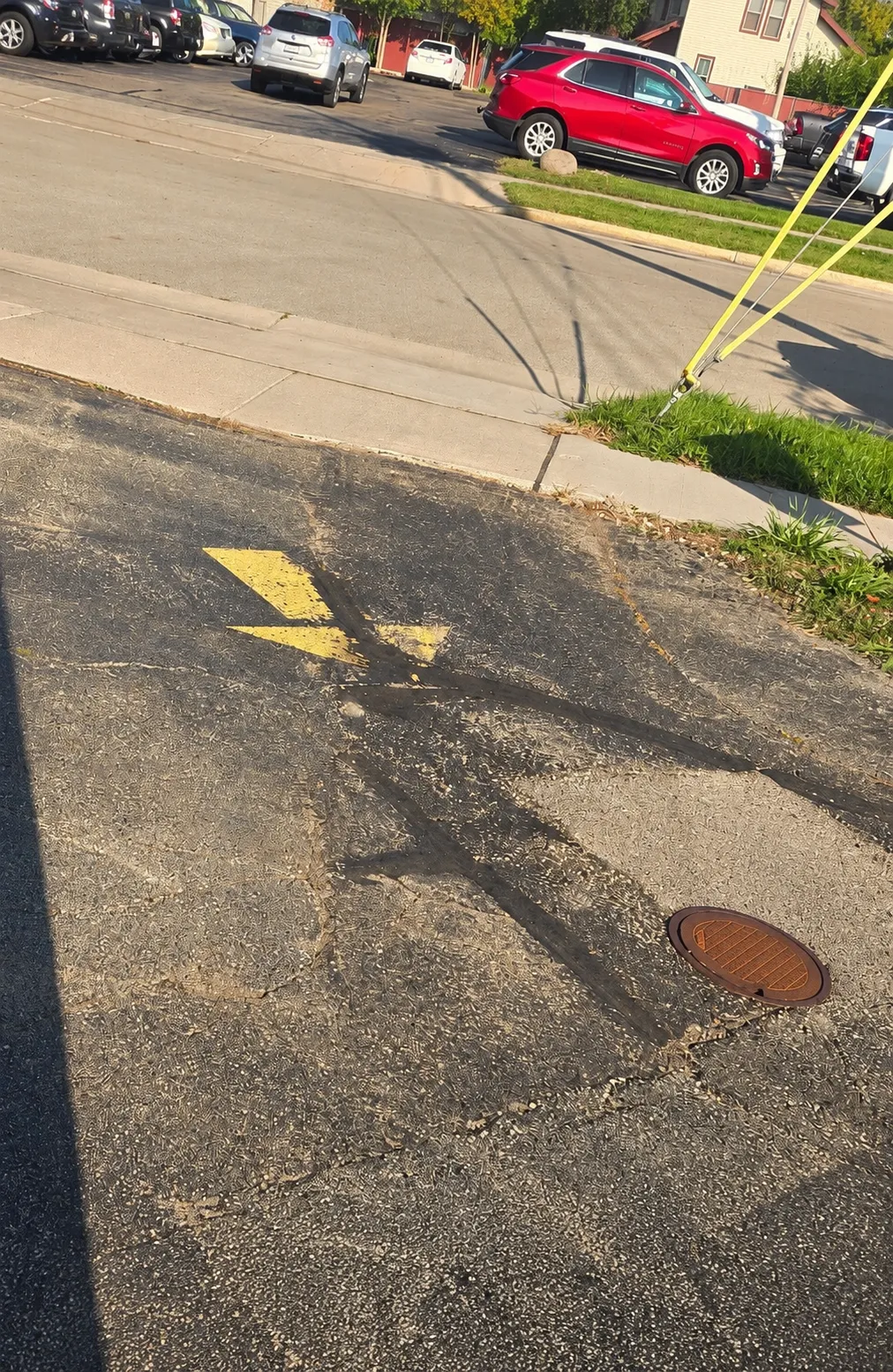 Worn asphalt pavement with faded directional markings, crack repairs, and a utility access cover