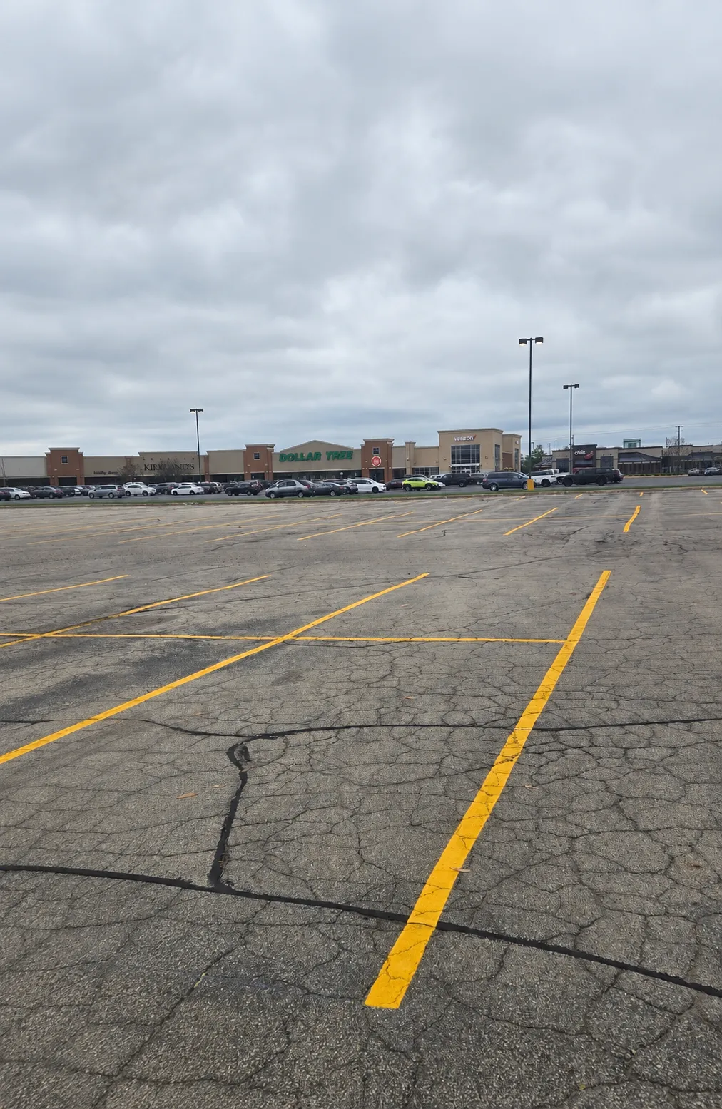 Commercial parking lot with fresh yellow striping and sealed cracks across aging asphalt pavement.
