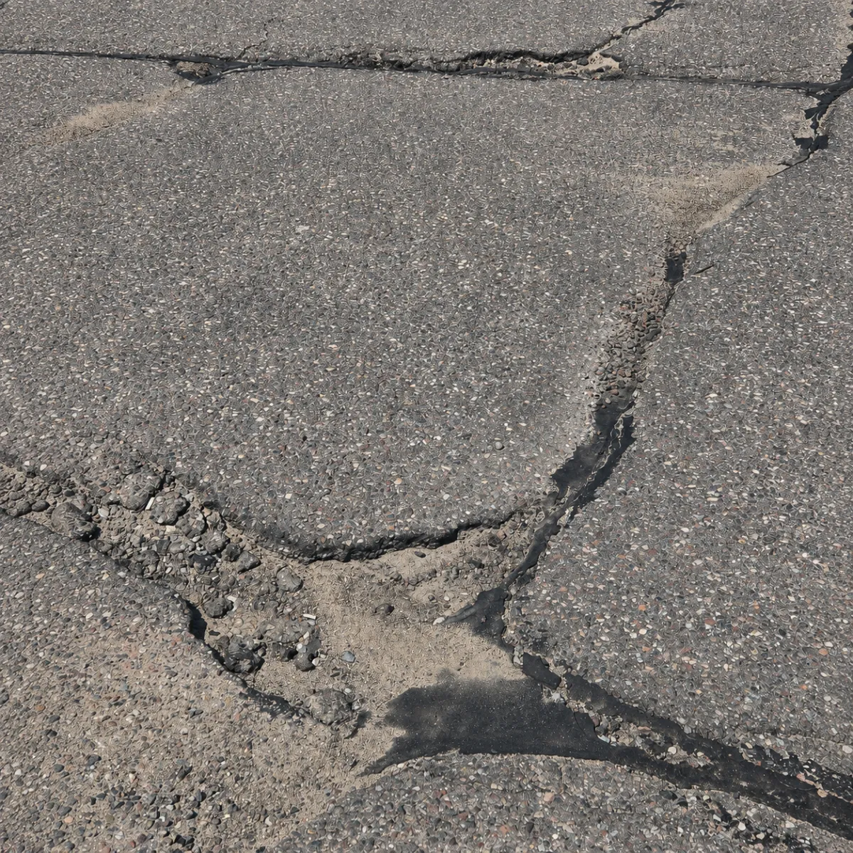 Deteriorated asphalt pavement with wide cracking, loose aggregate, and a localized failed repair area