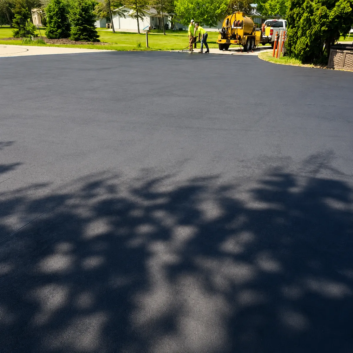 Freshly sealcoated asphalt surface with a pavement maintenance crew and sealcoating equipment in the background.