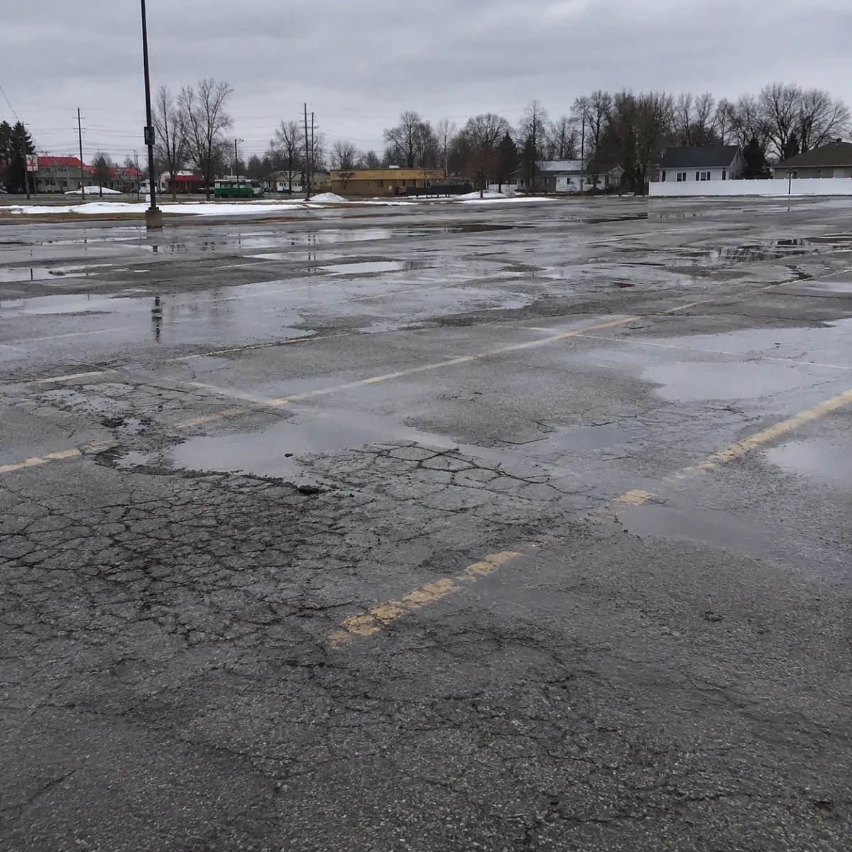 Deteriorated parking lot pavement with extensive cracking, standing water, and poor surface drainage