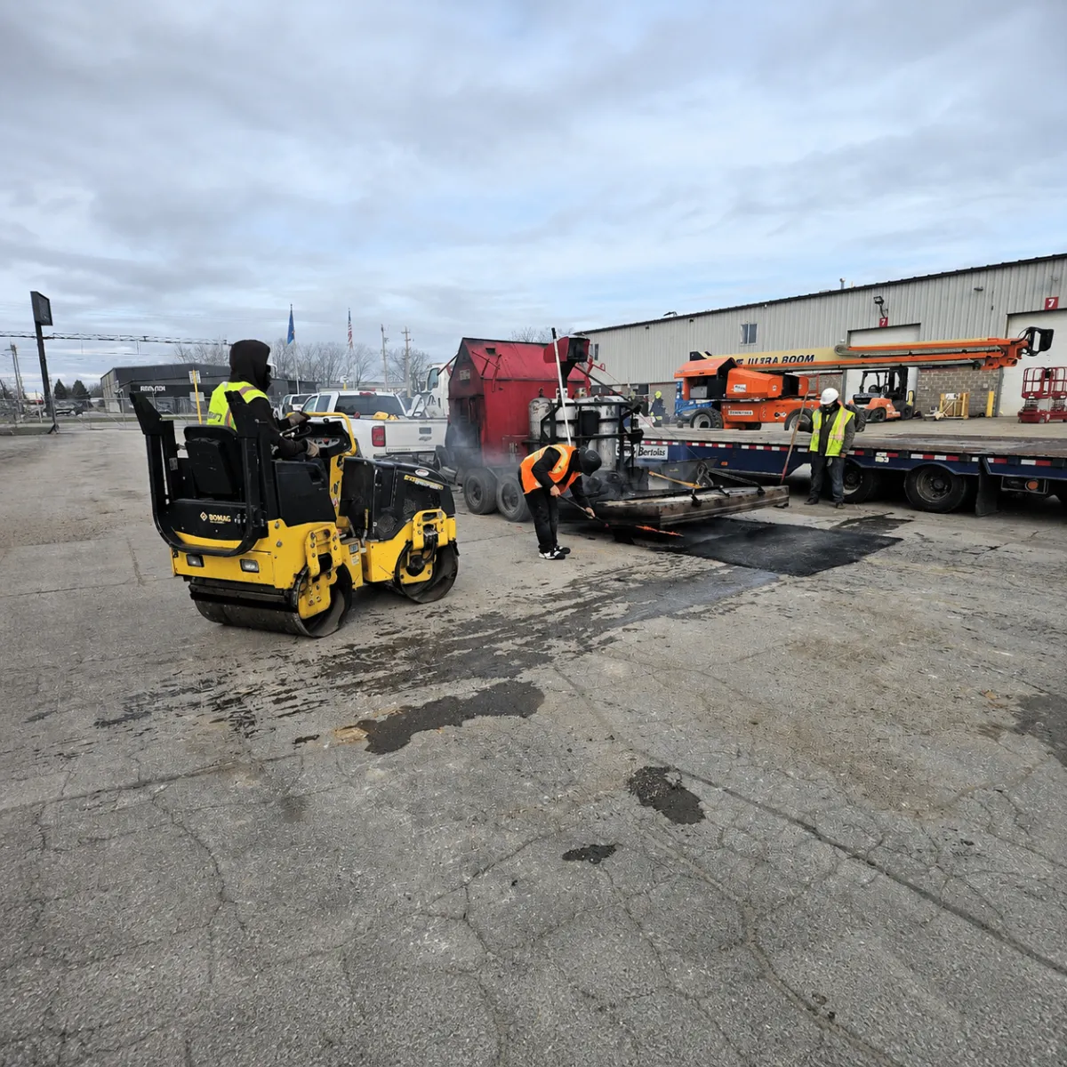 Crew performing commercial asphalt patching with a roller and hot asphalt repair equipment.