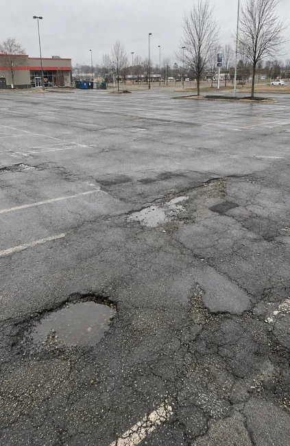 Damaged asphalt parking lot with potholes, cracking, standing water, and deteriorated pavement in Wisconsin