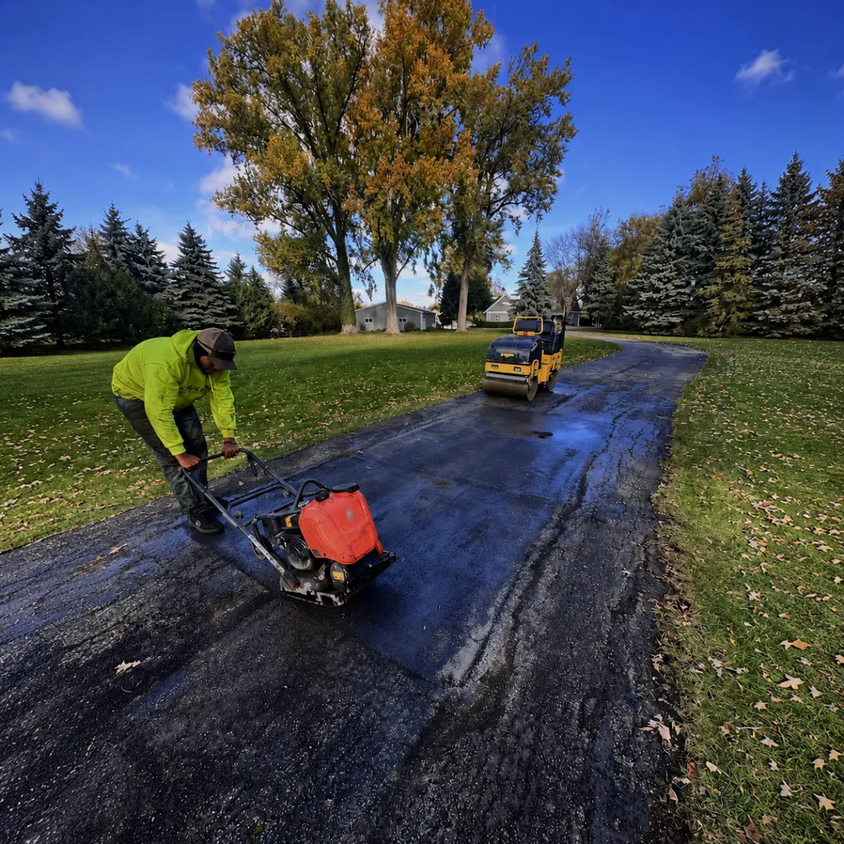 Worker compacting a newly repaired asphalt patch with a plate compactor and roller in Wisconsin