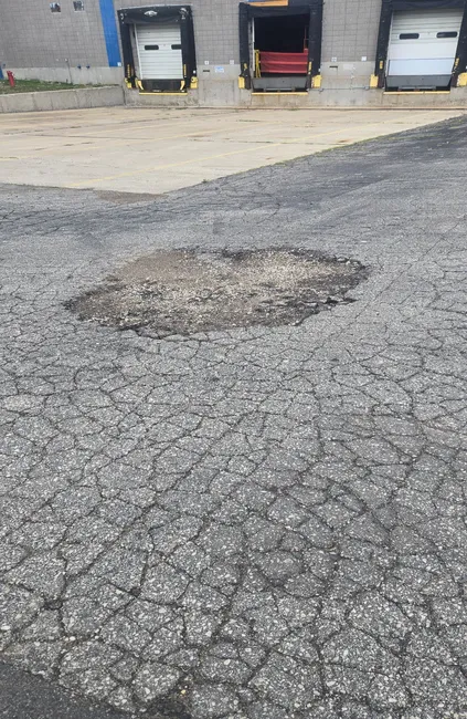 Large pothole and deteriorated asphalt pavement near commercial loading docks in Wisconsin
