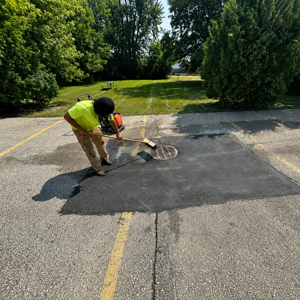 Worker repairing asphalt around a catch basin in a parking lot in Wisconsin