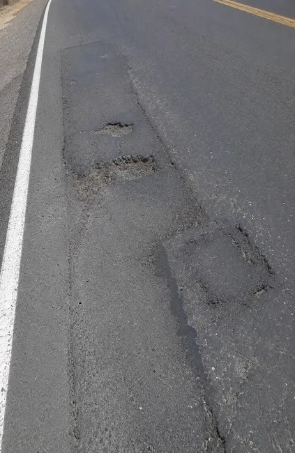 Failed asphalt patch with potholes, cracking, and deteriorated repair seams on a Wisconsin roadway