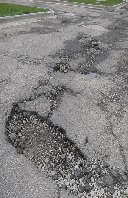 Severely deteriorated asphalt with potholes, broken pavement, and exposed base material in Wisconsin