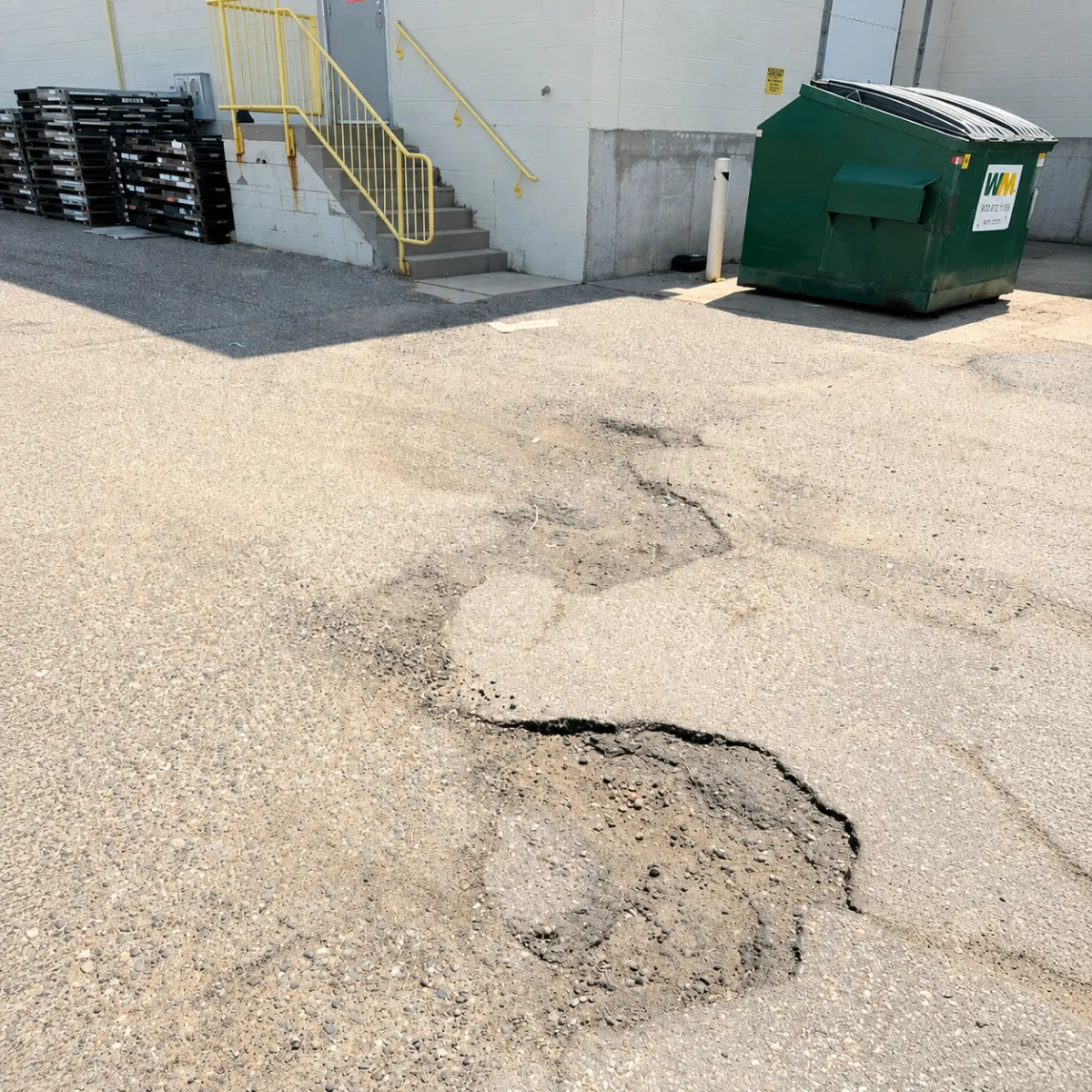 Multiple potholes and deteriorated asphalt pavement near a commercial building in Wisconsin