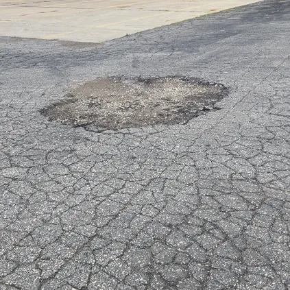 Severe asphalt pavement failure with cracking and a large pothole near commercial loading docks in Wisconsin