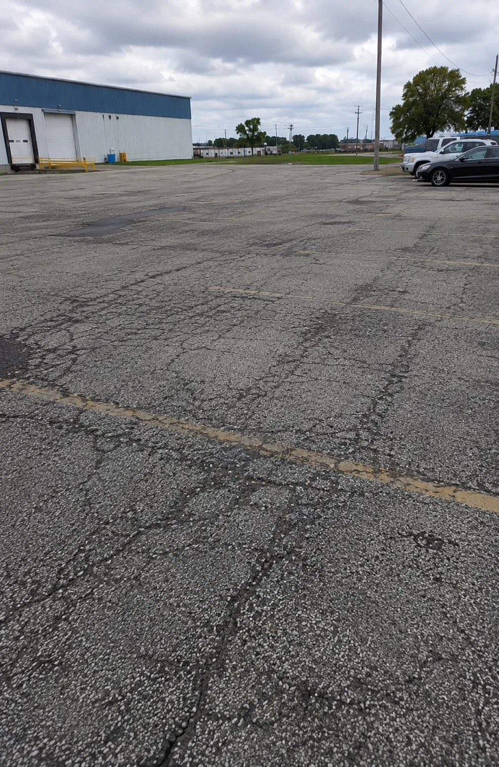 Deteriorated commercial parking lot pavement with widespread cracking, faded striping, and a storm drain.