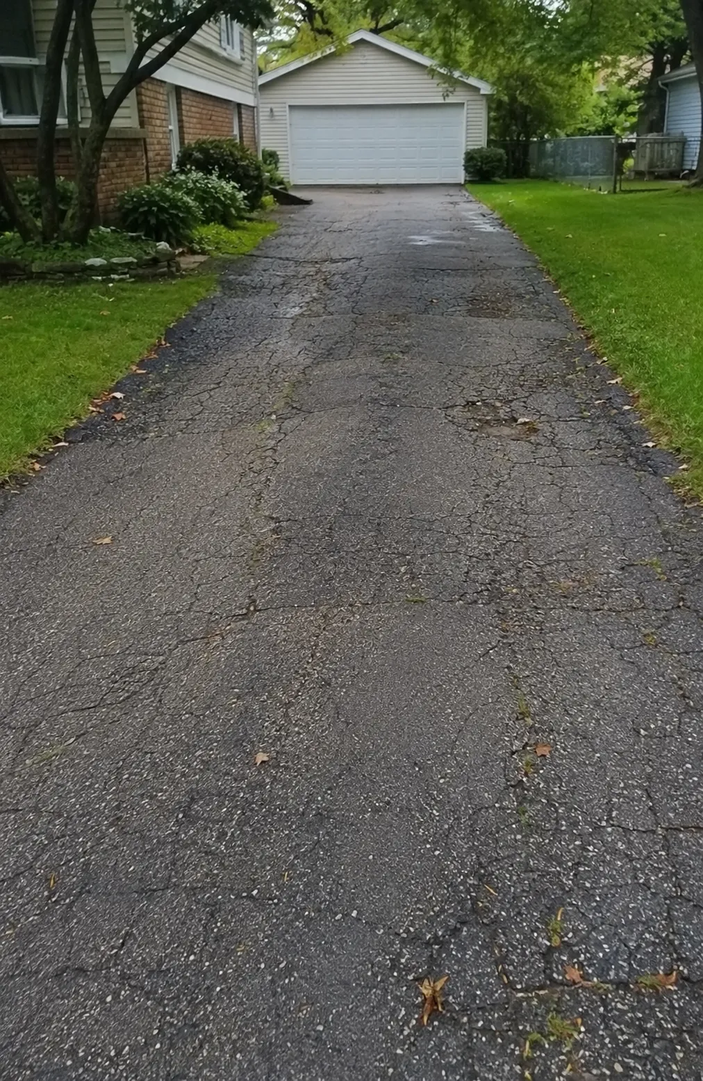 Cracked and deteriorated residential asphalt driveway leading to a detached garage