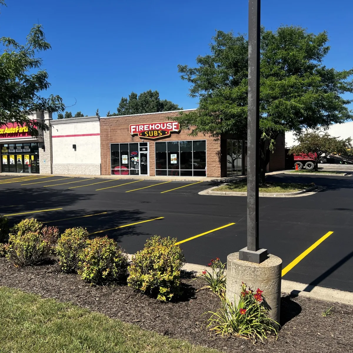 Freshly paved commercial parking lot with bright yellow striping in front of retail storefronts.