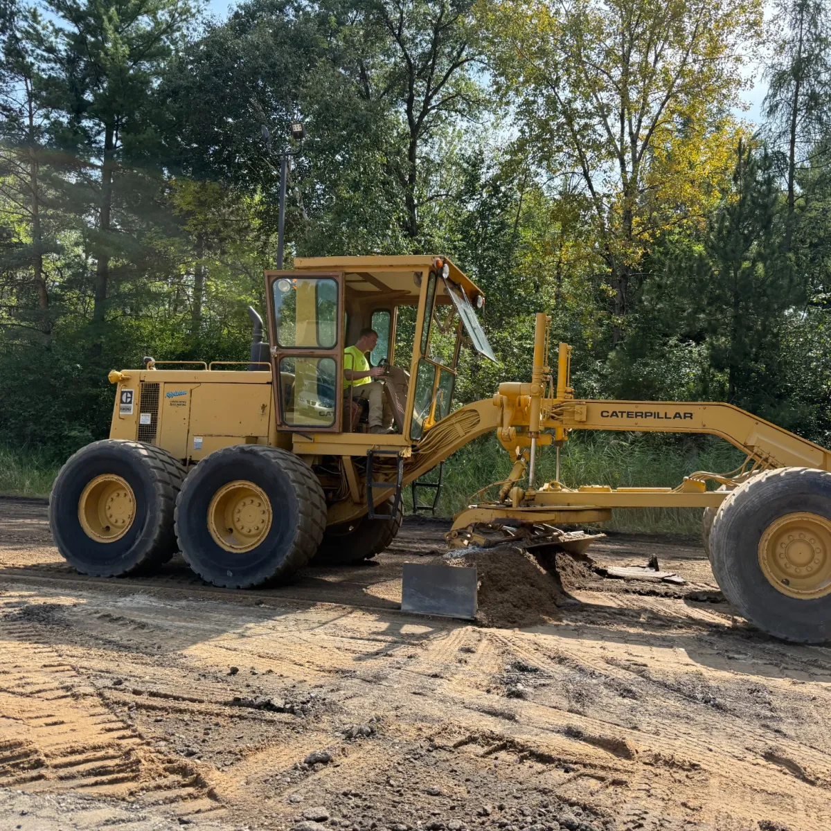 Grader leveling and preparing the aggregate base for asphalt paving.