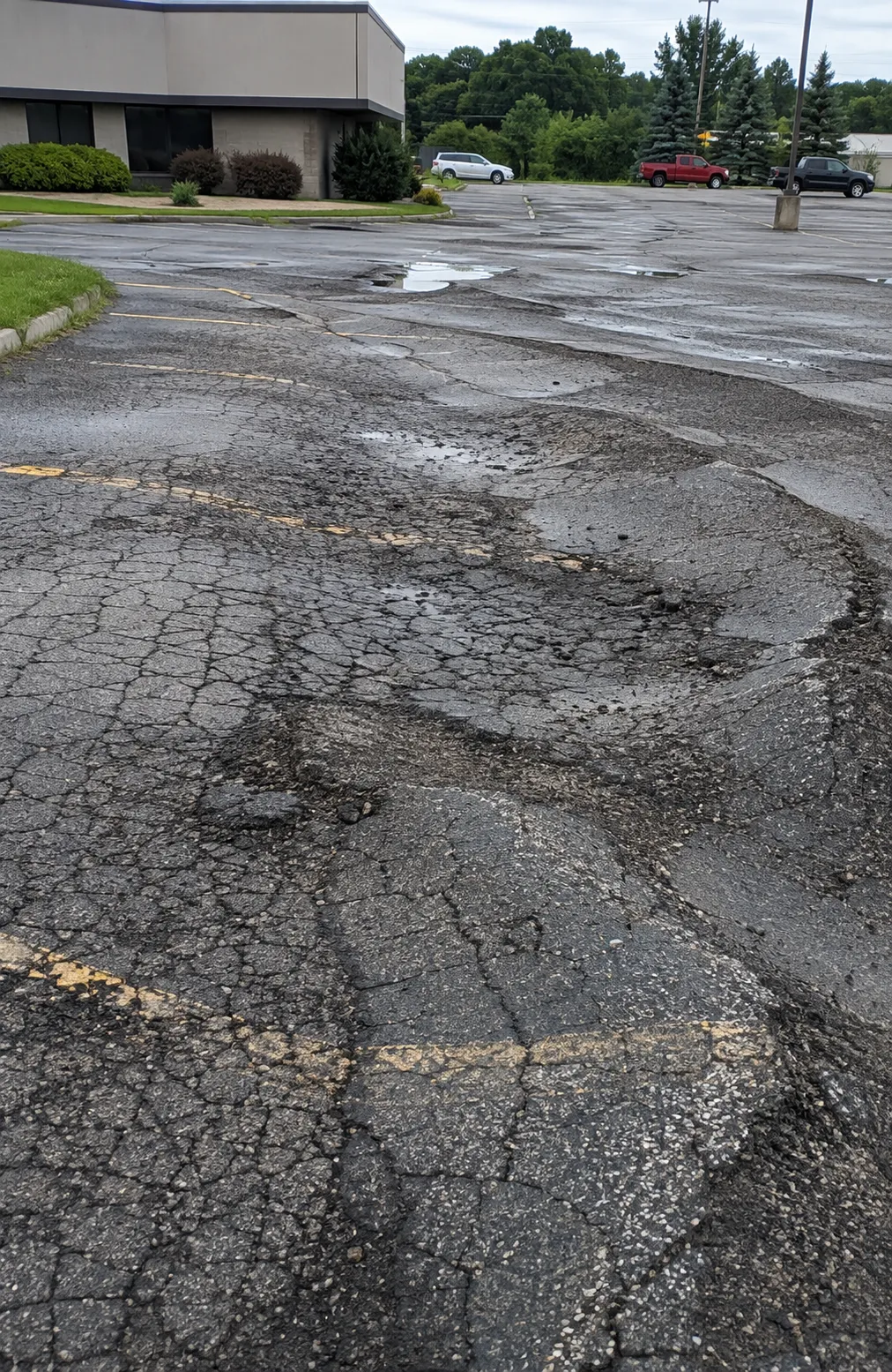 Severely deteriorated commercial parking lot pavement with extensive cracking, potholes, and standing water.