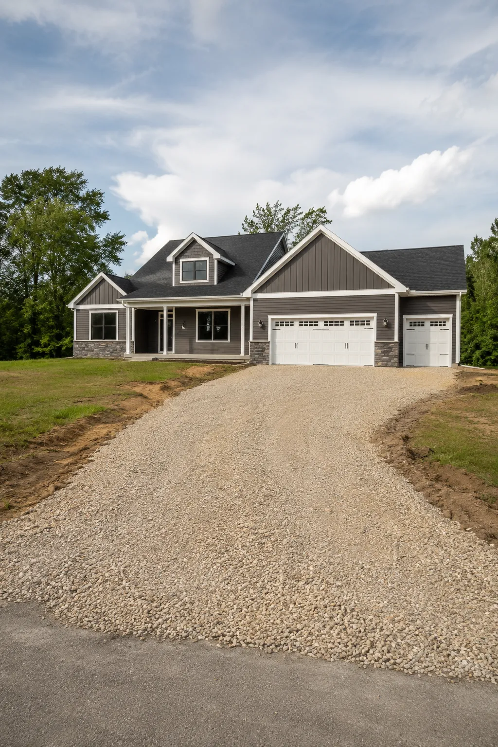 Newly built home with a graded gravel driveway base prepared for asphalt paving.