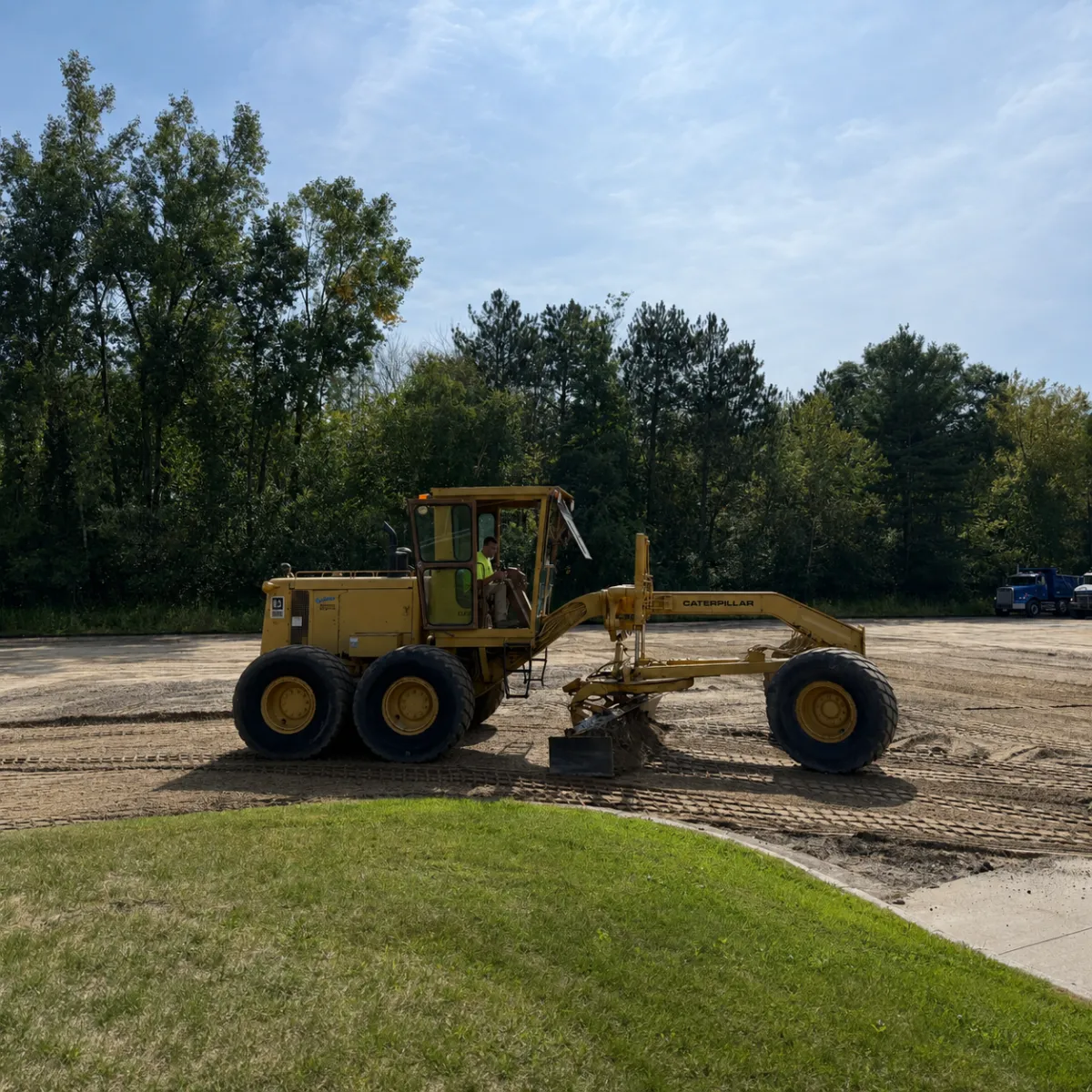 Motor grader and crew leveling the aggregate base during commercial parking lot preparation for asphalt paving