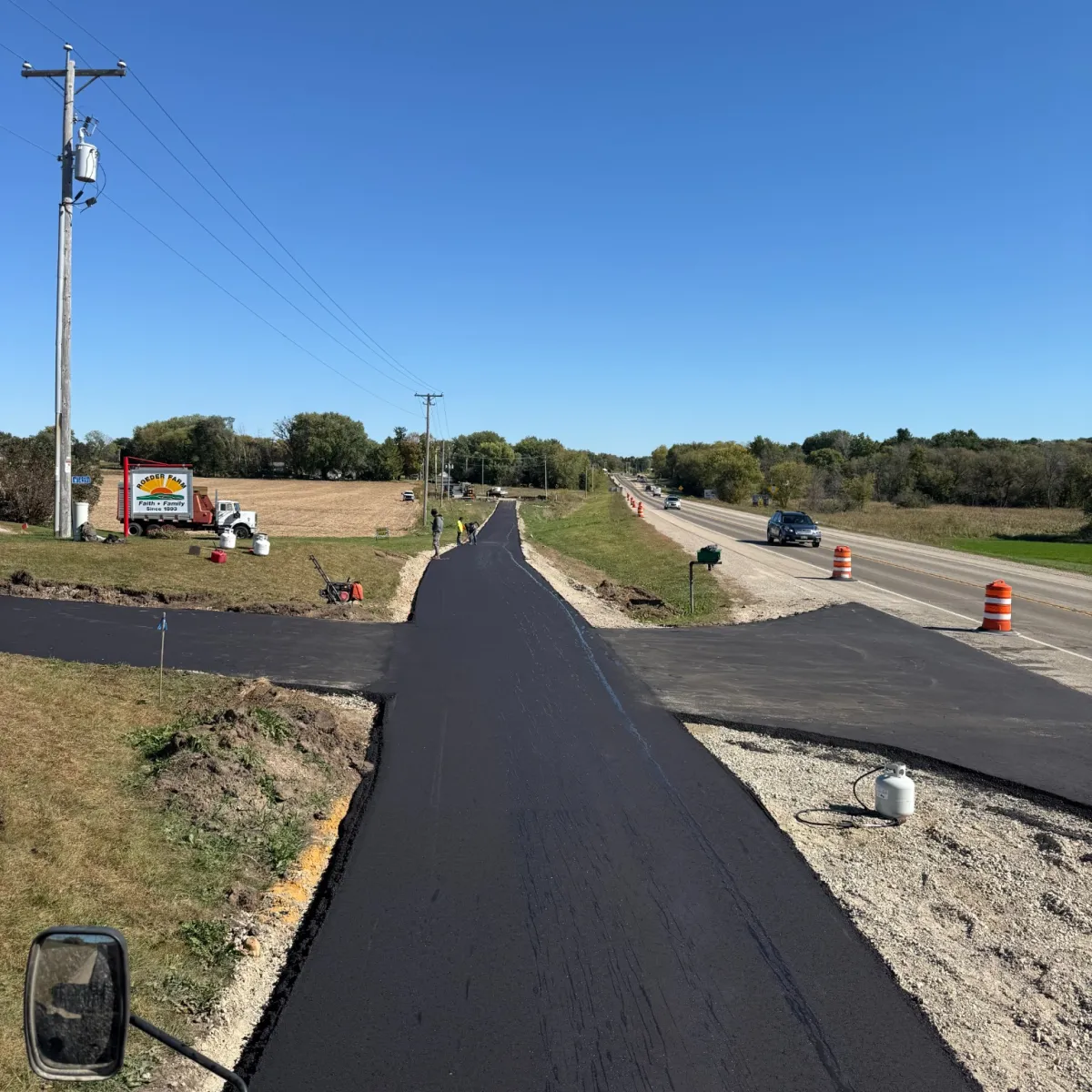 Newly paved private asphalt road with fresh driveway connections beside a rural roadway.