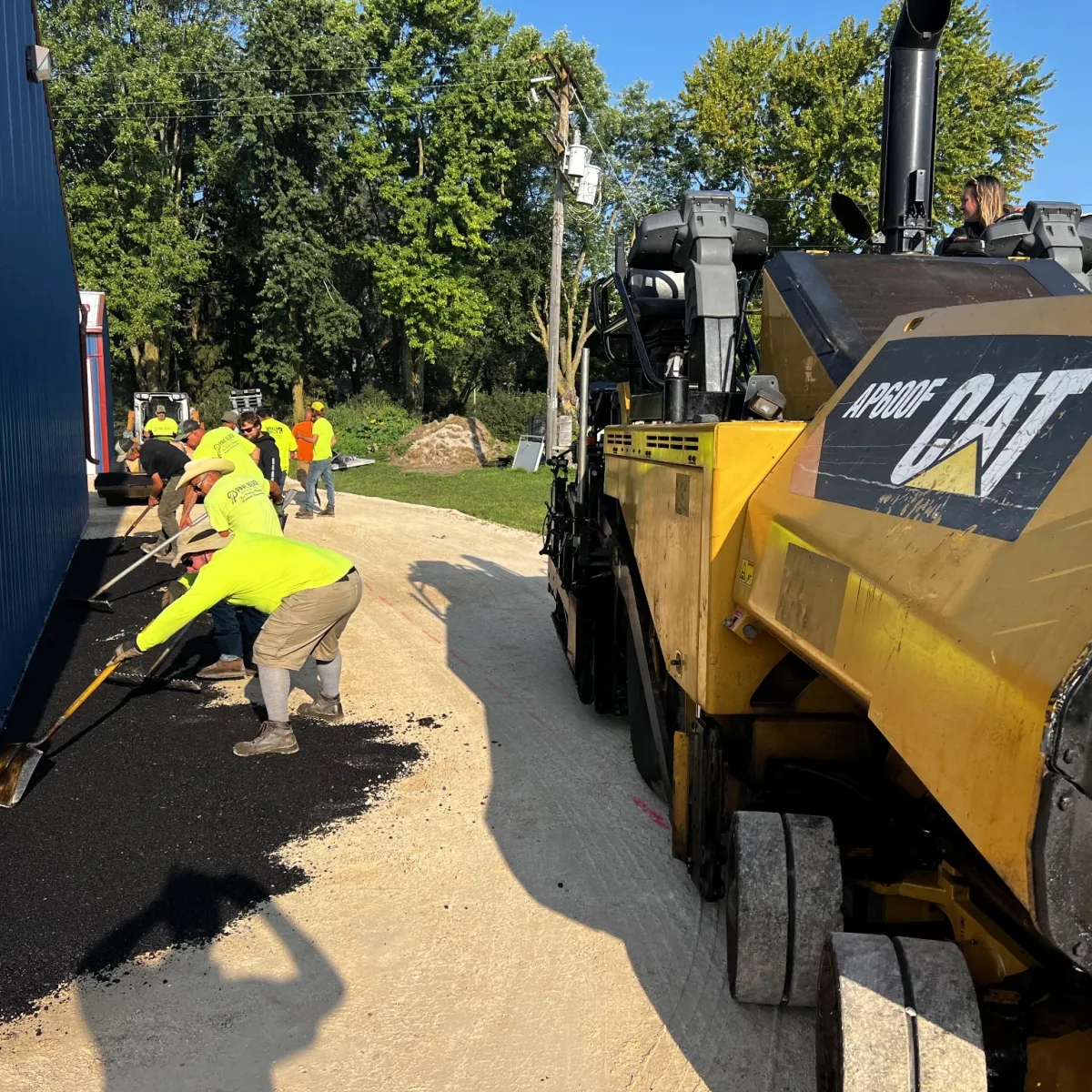 Asphalt paving crew placing fresh pavement beside a commercial building with a paving machine.