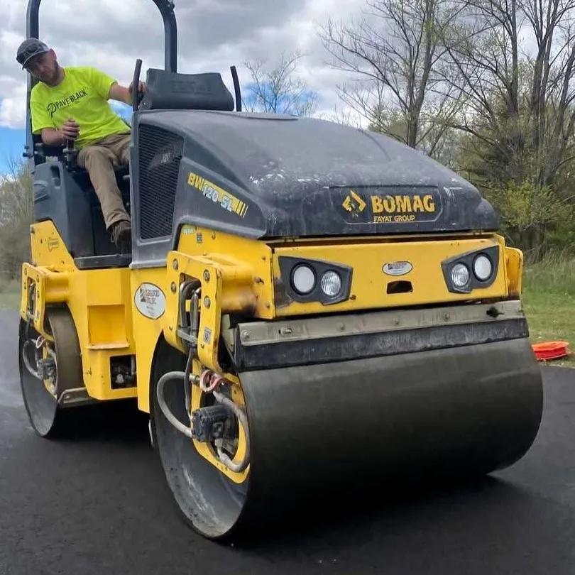 Paving crew member operating a roller to compact freshly placed asphalt pavement.