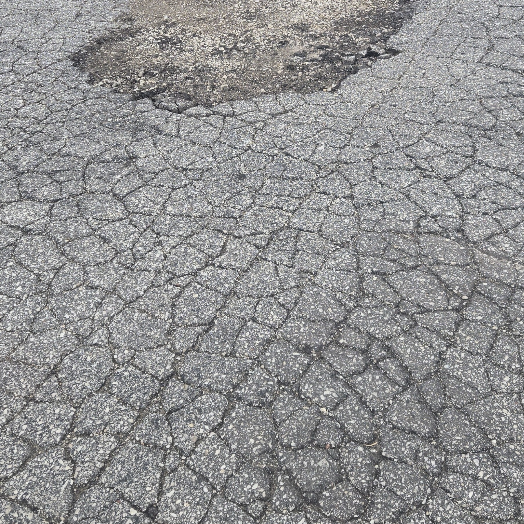 Commercial asphalt pavement with widespread cracking and a large localized surface failure near loading docks.