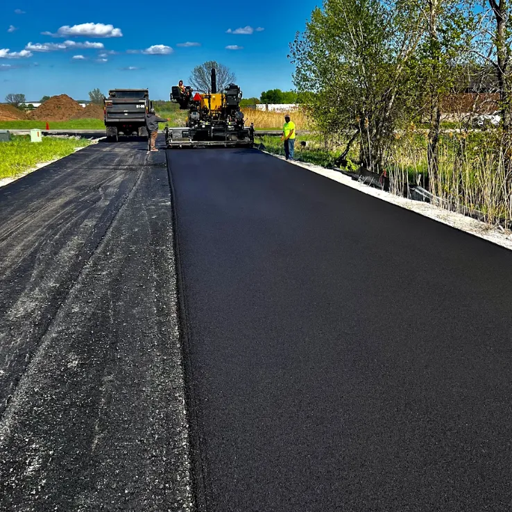 Asphalt paving crew placing fresh pavement over lay on a new roadway with a paver and dump truck