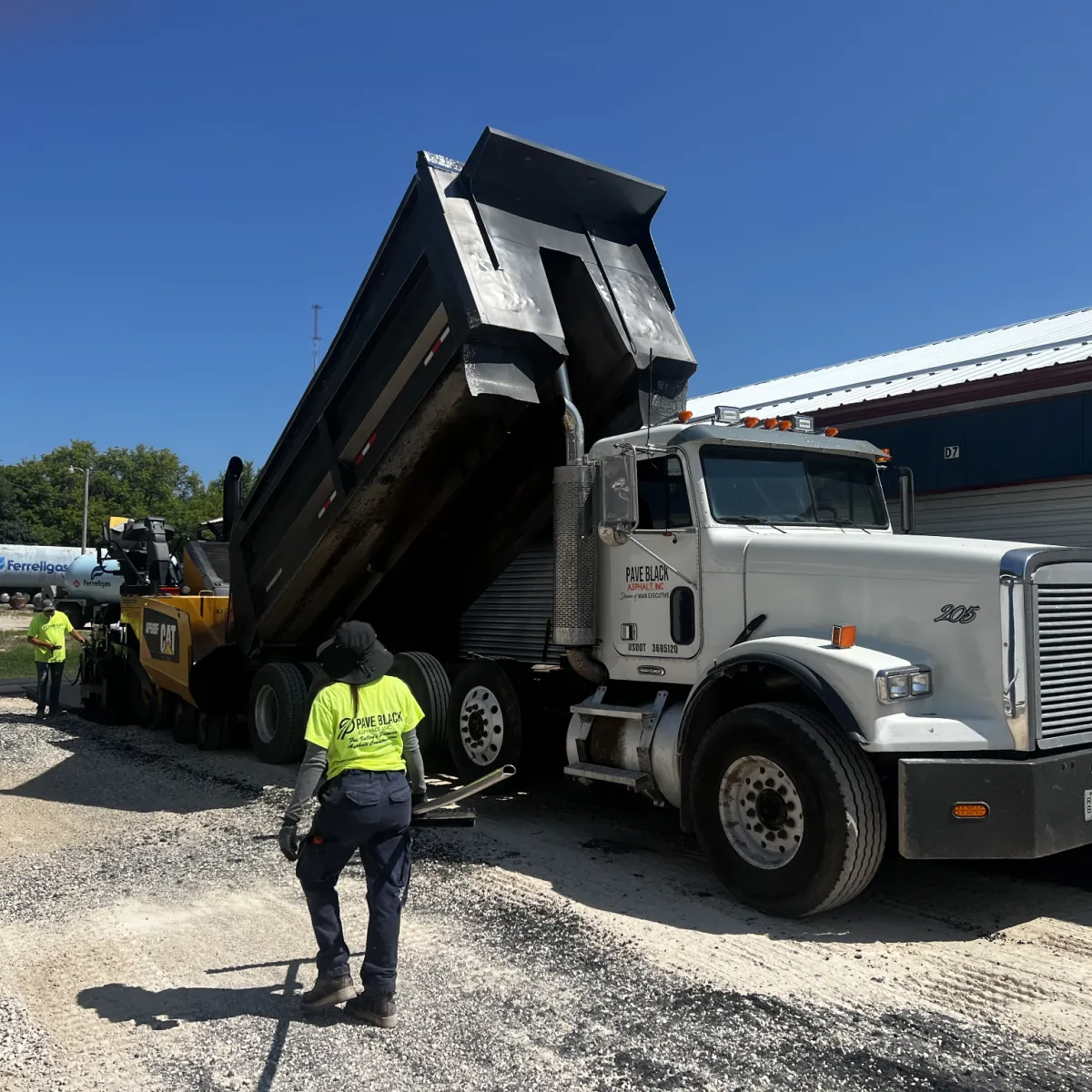 Asphalt paving crew feeding hot mix from a dump truck into a paver during a commercial paving project.