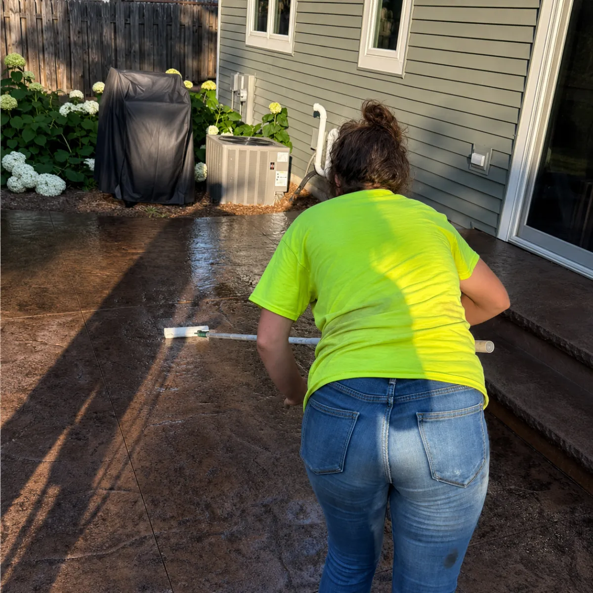 Worker applying concrete sealer to a stamped concrete patio beside a home.