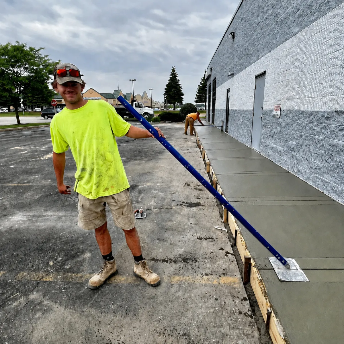 Concrete crew finishing a freshly poured commercial concrete sidewalk beside a building.