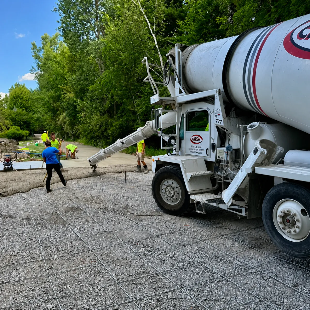 Concrete crew pouring reinforced concrete over a prepared gravel base with rebar using a ready-mix truck.