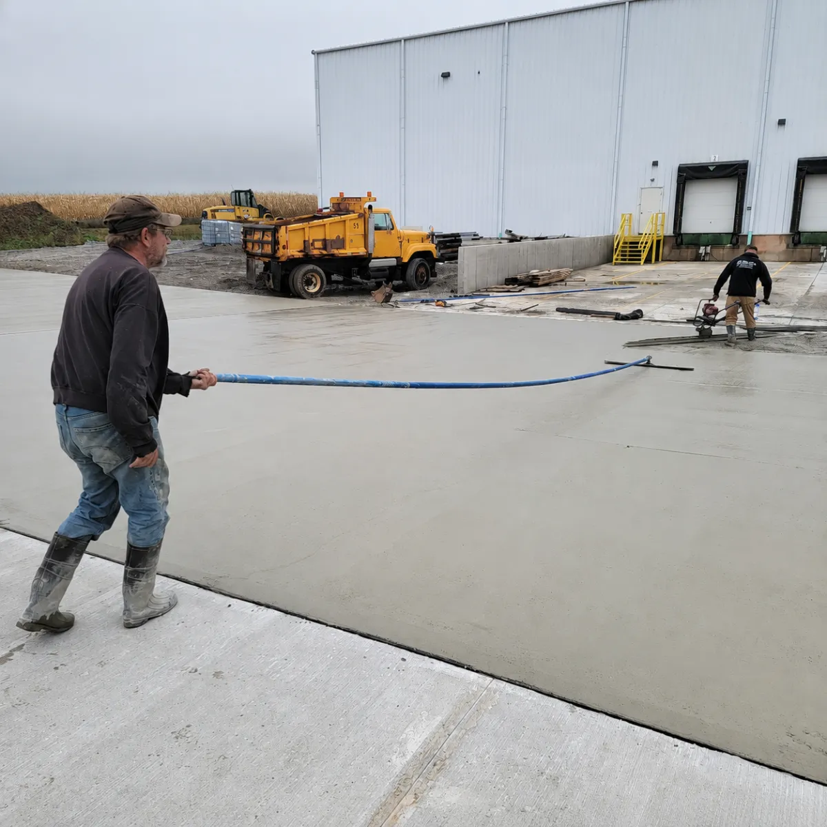 Concrete crew finishing freshly poured commercial pavement beside an industrial loading dock.