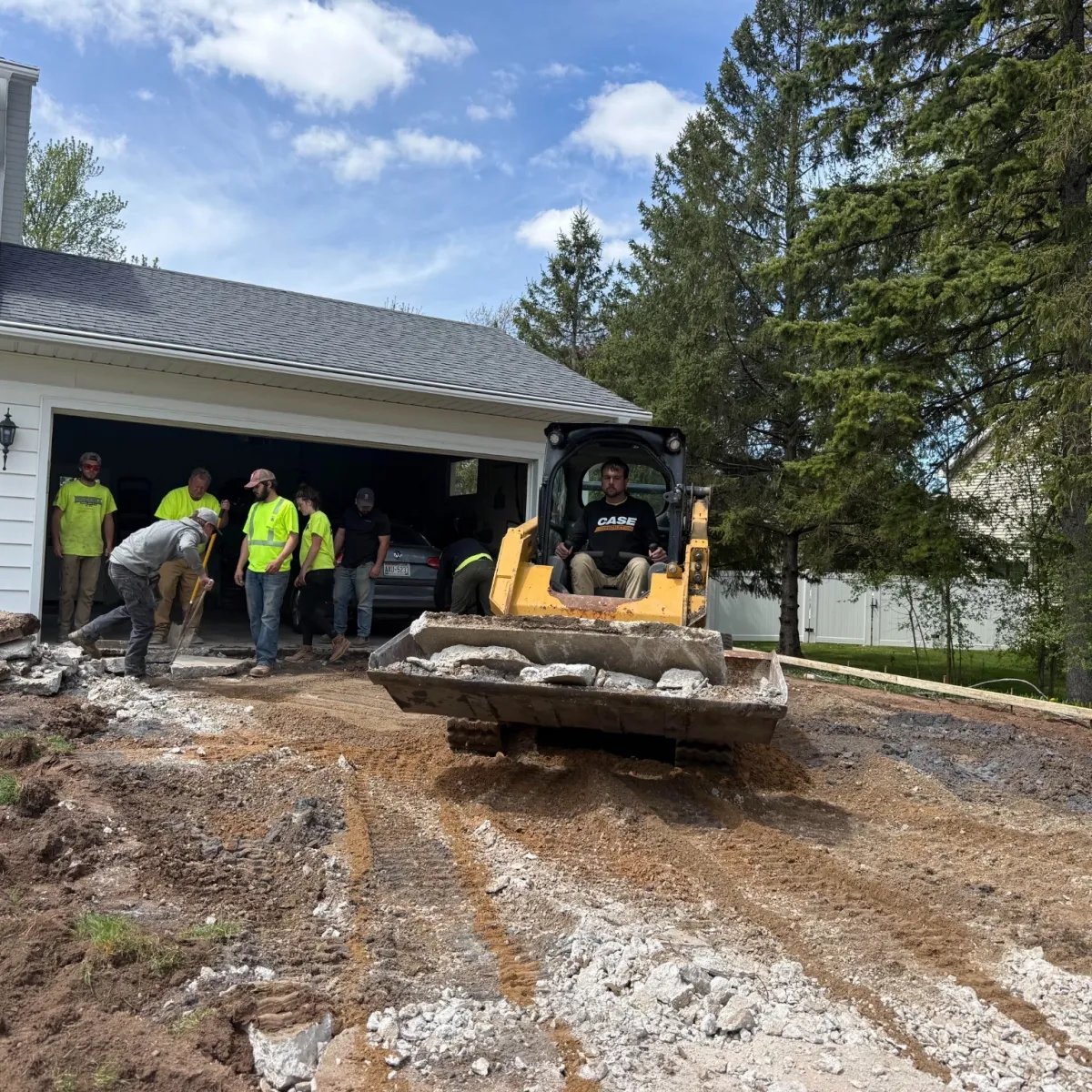 Crew removing a damaged concrete driveway with a skid steer during residential concrete replacement.