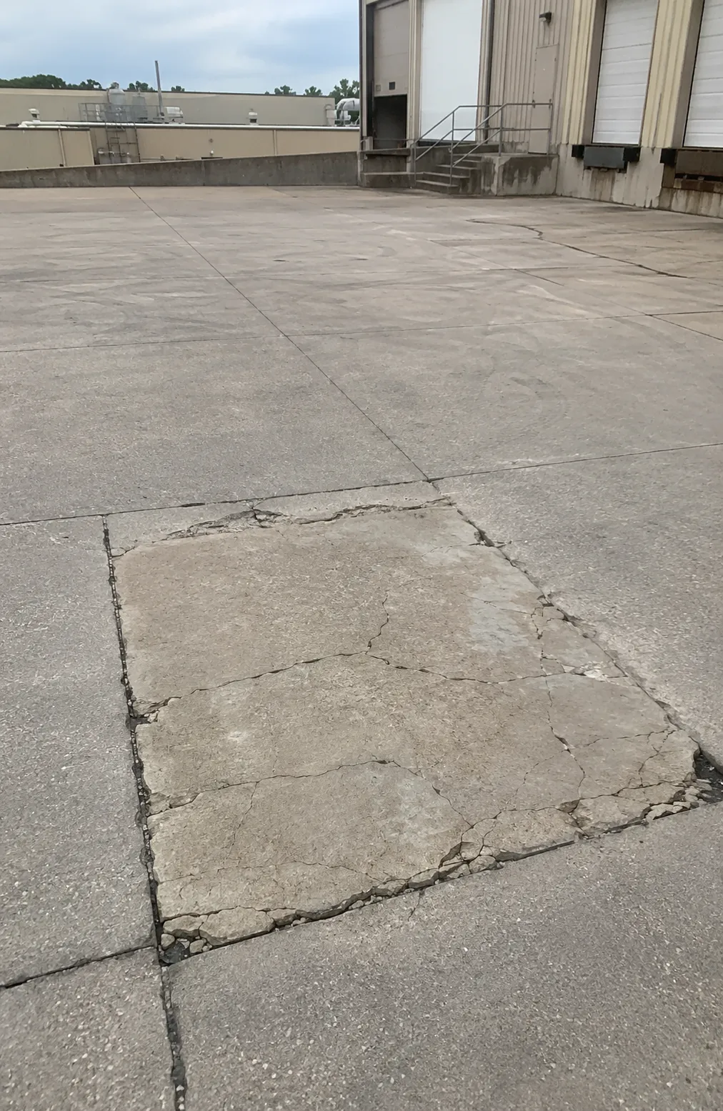 Cracked and deteriorated concrete slab in a commercial loading area with broken edges and surface failure.