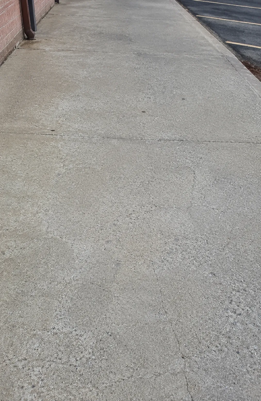Existing commercial concrete sidewalk with control joints and minor surface wear beside a building.