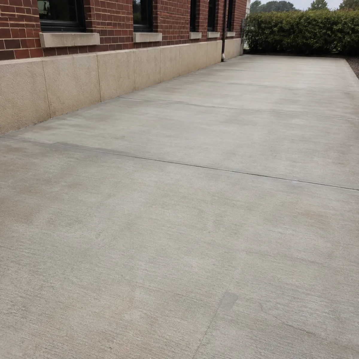 Newly replaced commercial concrete sidewalk with clean control joints beside a brick building.