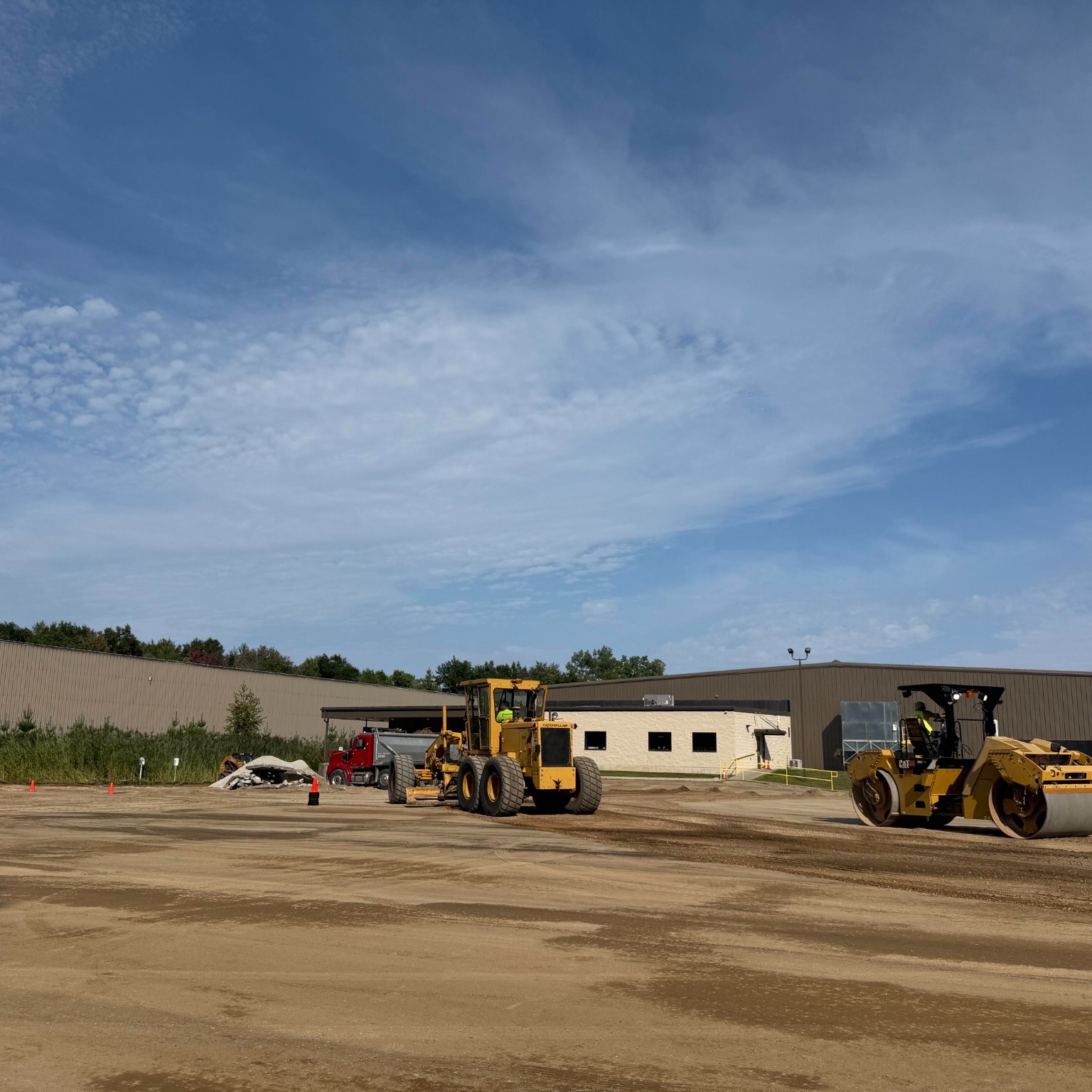 Heavy equipment grading and compacting the base for a large commercial pavement construction project.